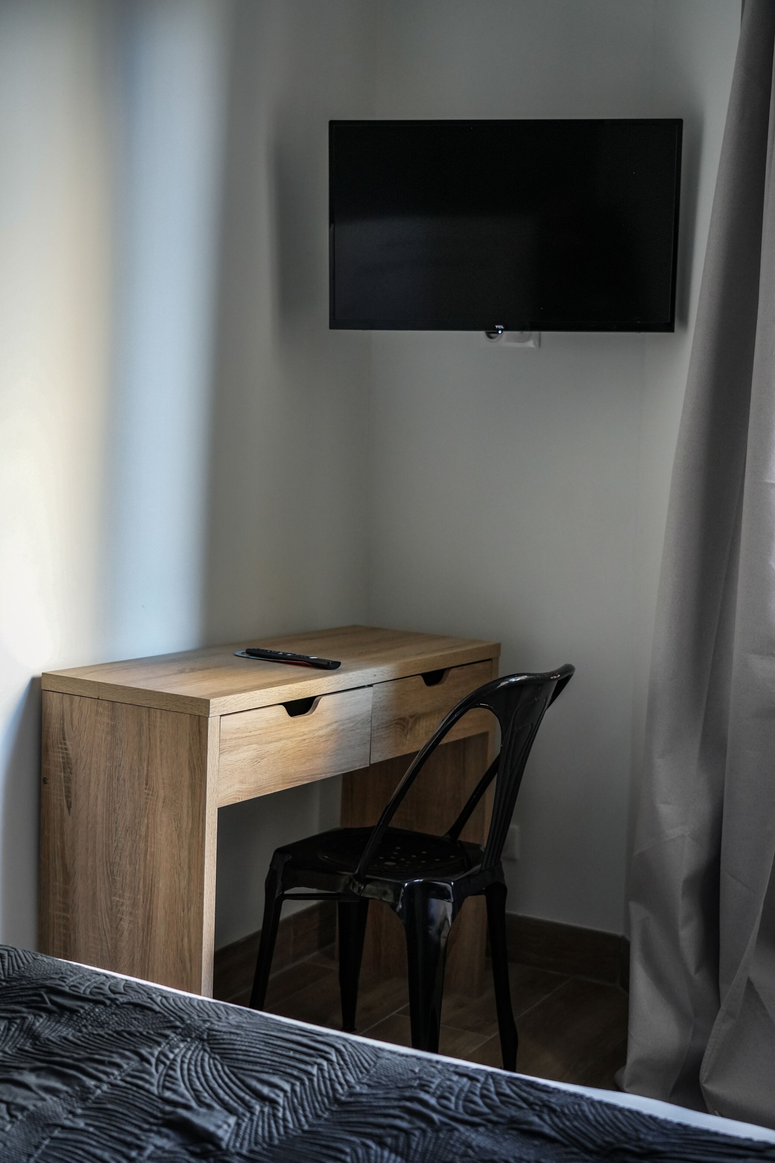 A small, neatly arranged bedroom with a wooden desk, a chair, a bed, and a TV mounted on the wall.