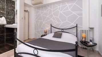 Une chambre moderne avec un mur orné d’un motif géométrique, un lit en métal noir, une table de chevet avec une lampe et un radiateur.