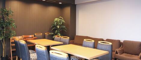 A modern conference room with wooden tables and chairs, a brown sofa, and a large plant.