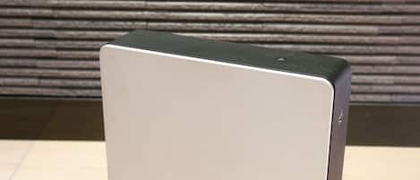 A modern, minimalist air purifier with a sleek design, placed on a wooden floor against a textured wall.