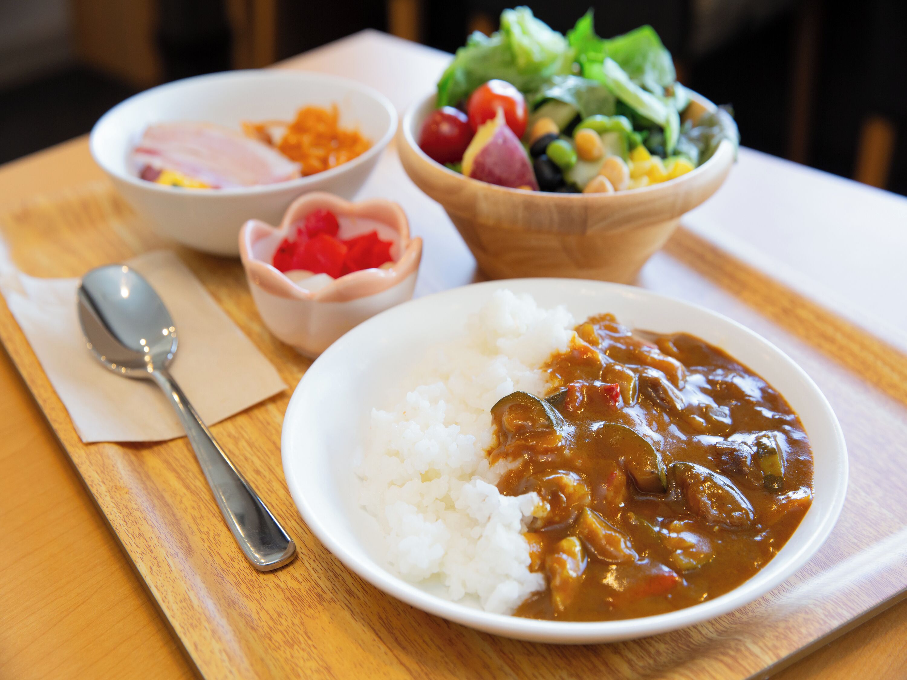 A meal with rice and curry, a salad, and a bowl of pickled vegetables on a wooden table.