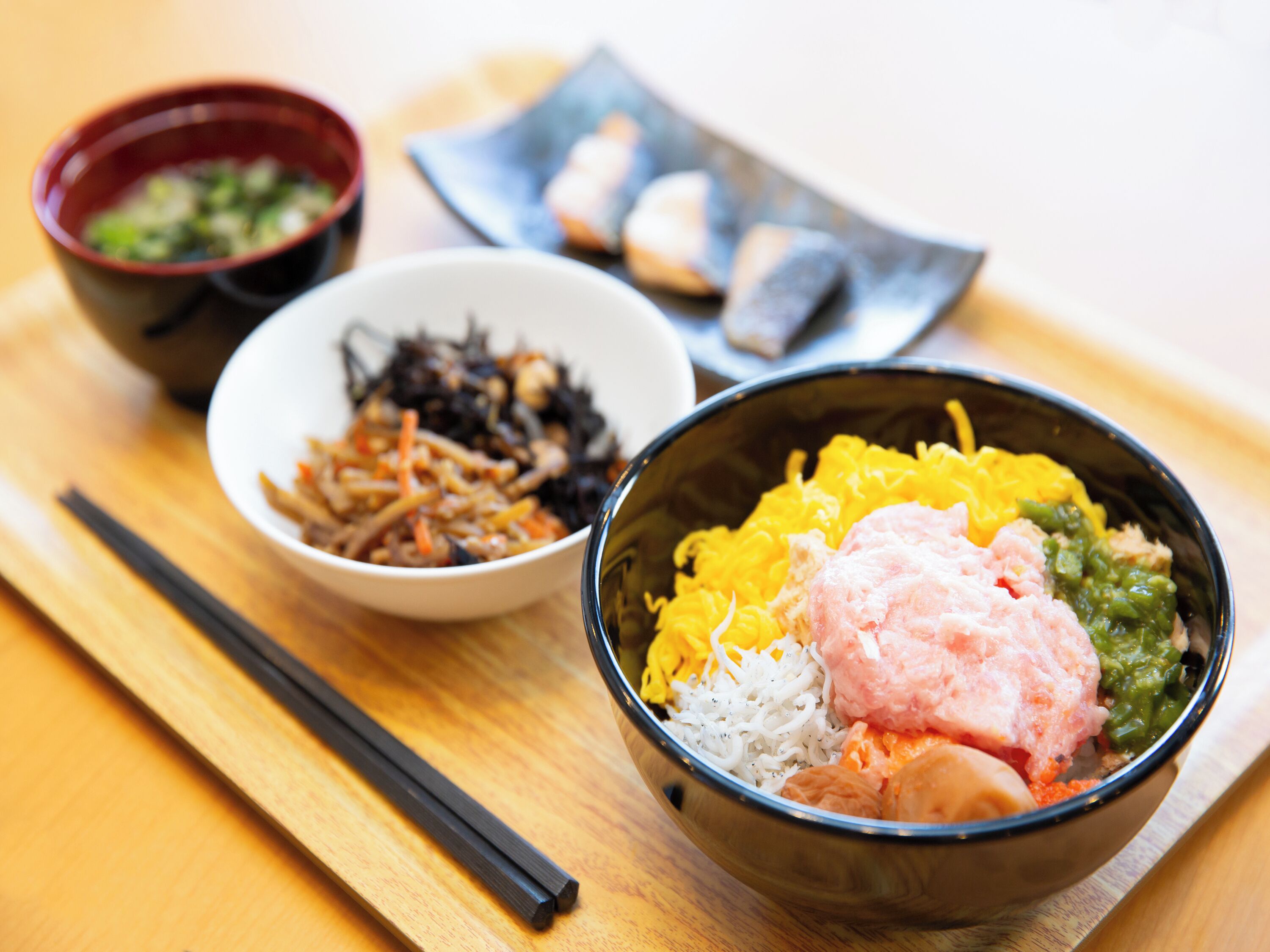 A wooden table with a bowl of colorful food, chopsticks, and two smaller bowls with different dishes.