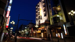 Hotel com vários andares, entrada visível e rua com carros passando.