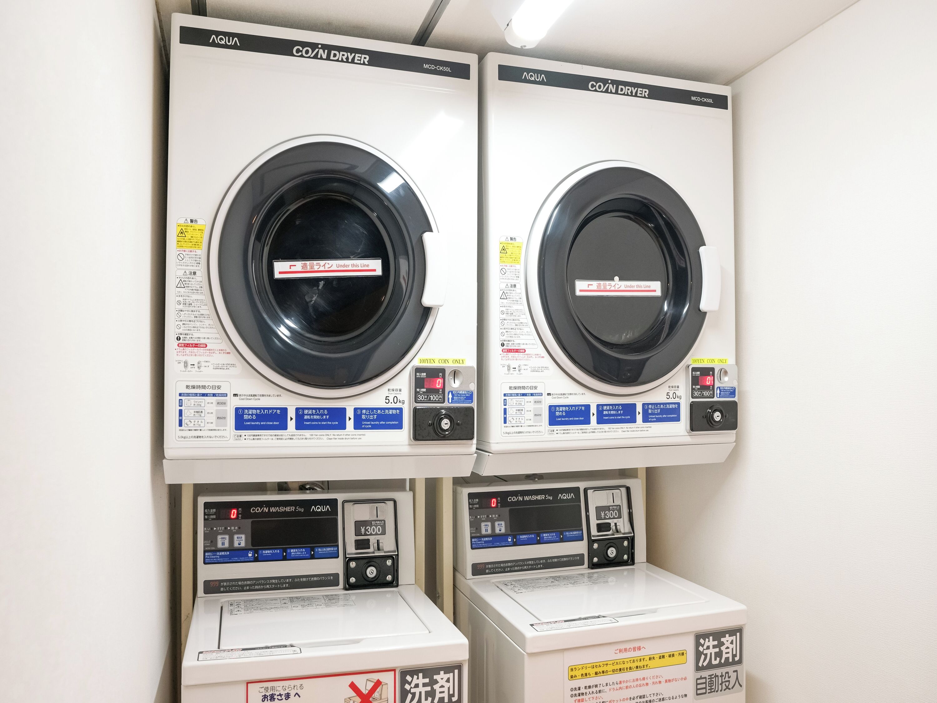Two co-in dryer machines with control panels and a co-in washer machine below them.