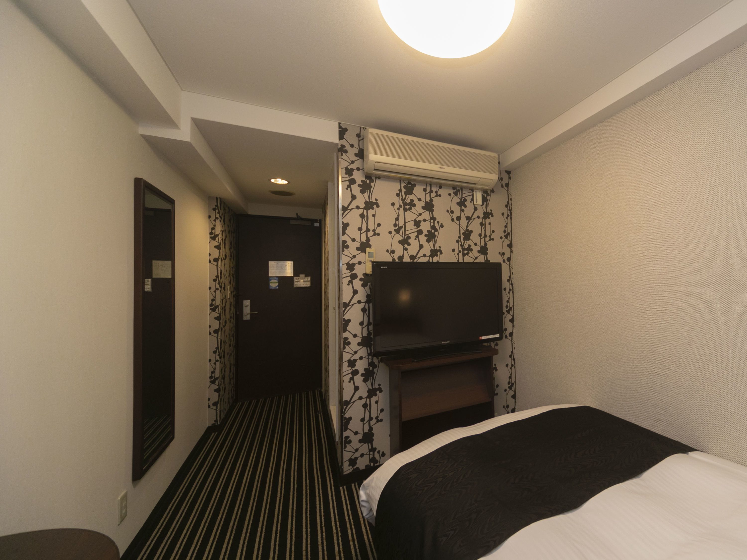 Een hotelkamer met een bed, een flatscreen televisie aan de muur, een plafondventilator en een deur naar een andere kamer.