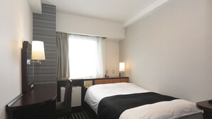 Quarto de hotel com cama, escrivaninha, cadeira, abajur e janela com cortinas.