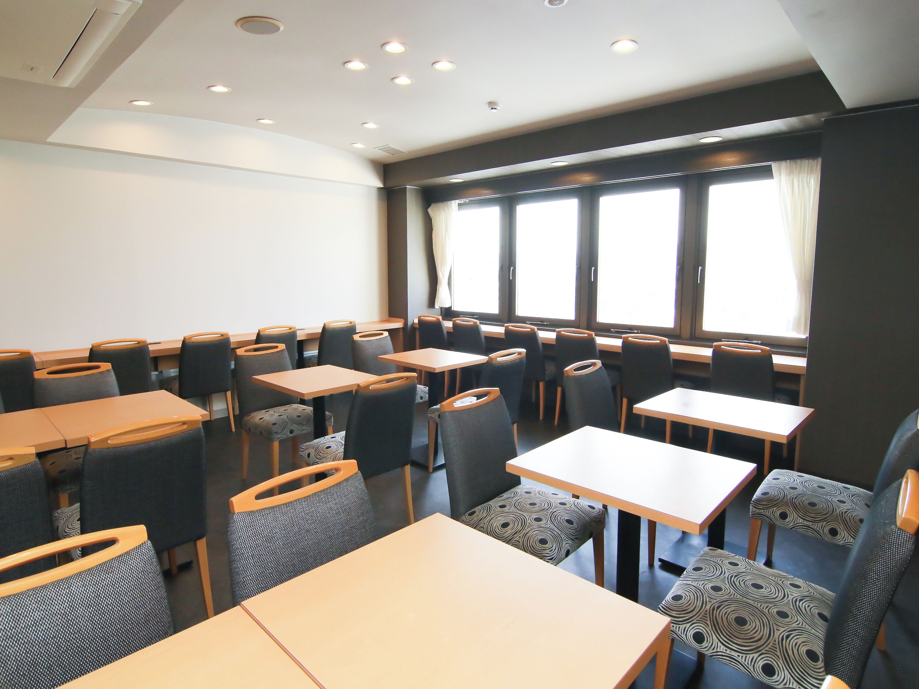 A conference room with multiple tables and chairs, large windows with curtains, and recessed ceiling lighting.
