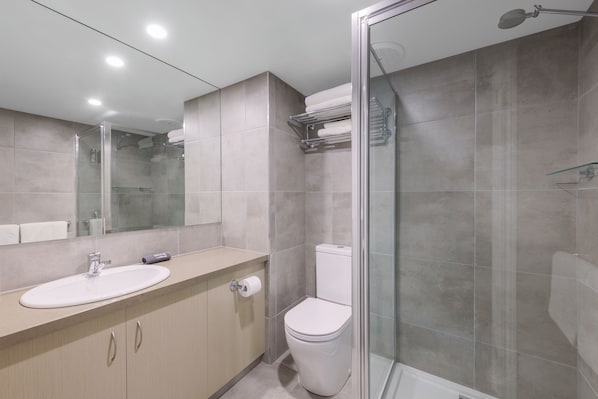 Un baño moderno con ducha de vidrio, lavamanos con espejo e inodoro.
