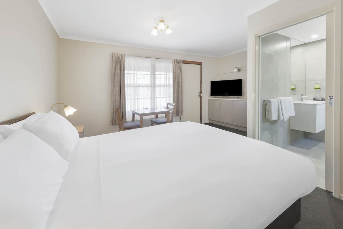 A hotel room with a large bed, a desk with a chair, a television, and a bathroom with a mirror and sink.