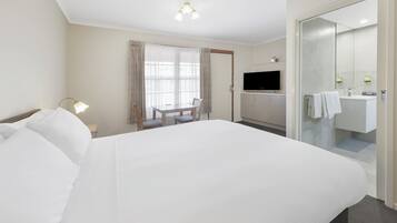 Habitación de hotel con una cama grande, un escritorio con silla, televisión y baño con espejo y lavamanos.