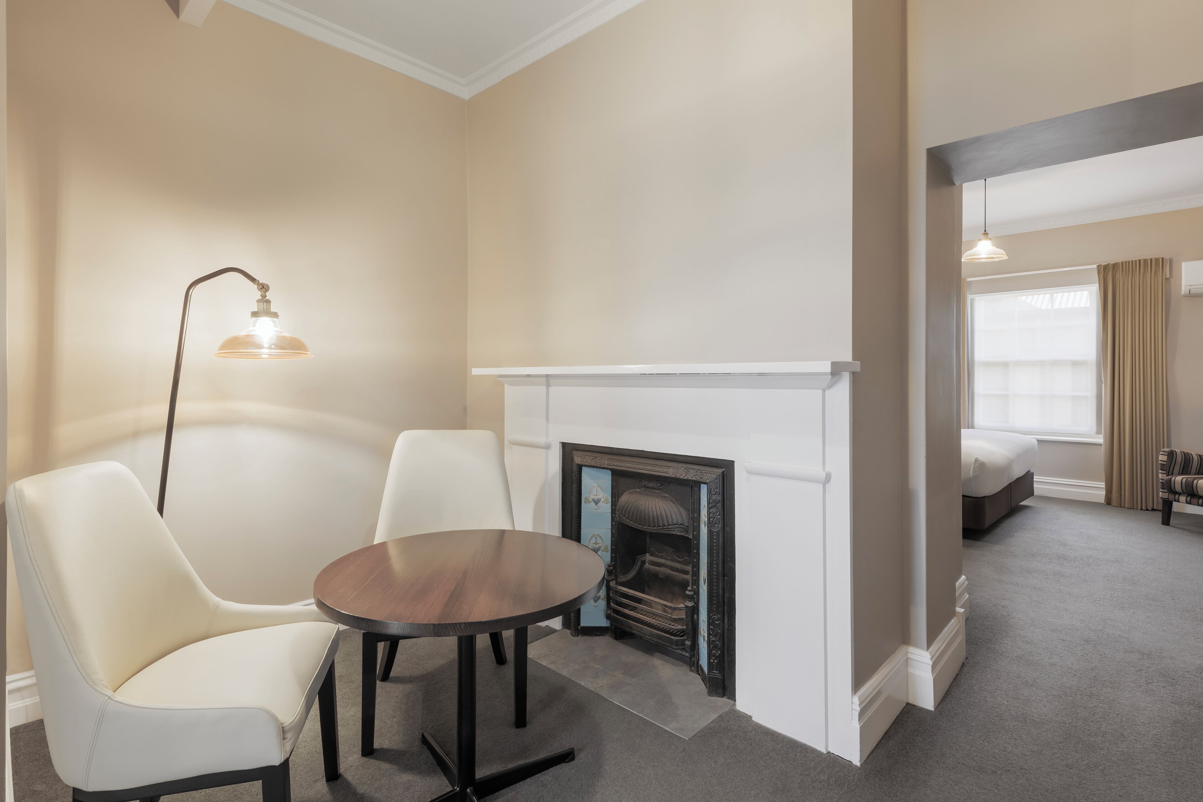 A hotel room with a fireplace, a round table, two chairs, a bed, and a window with curtains.