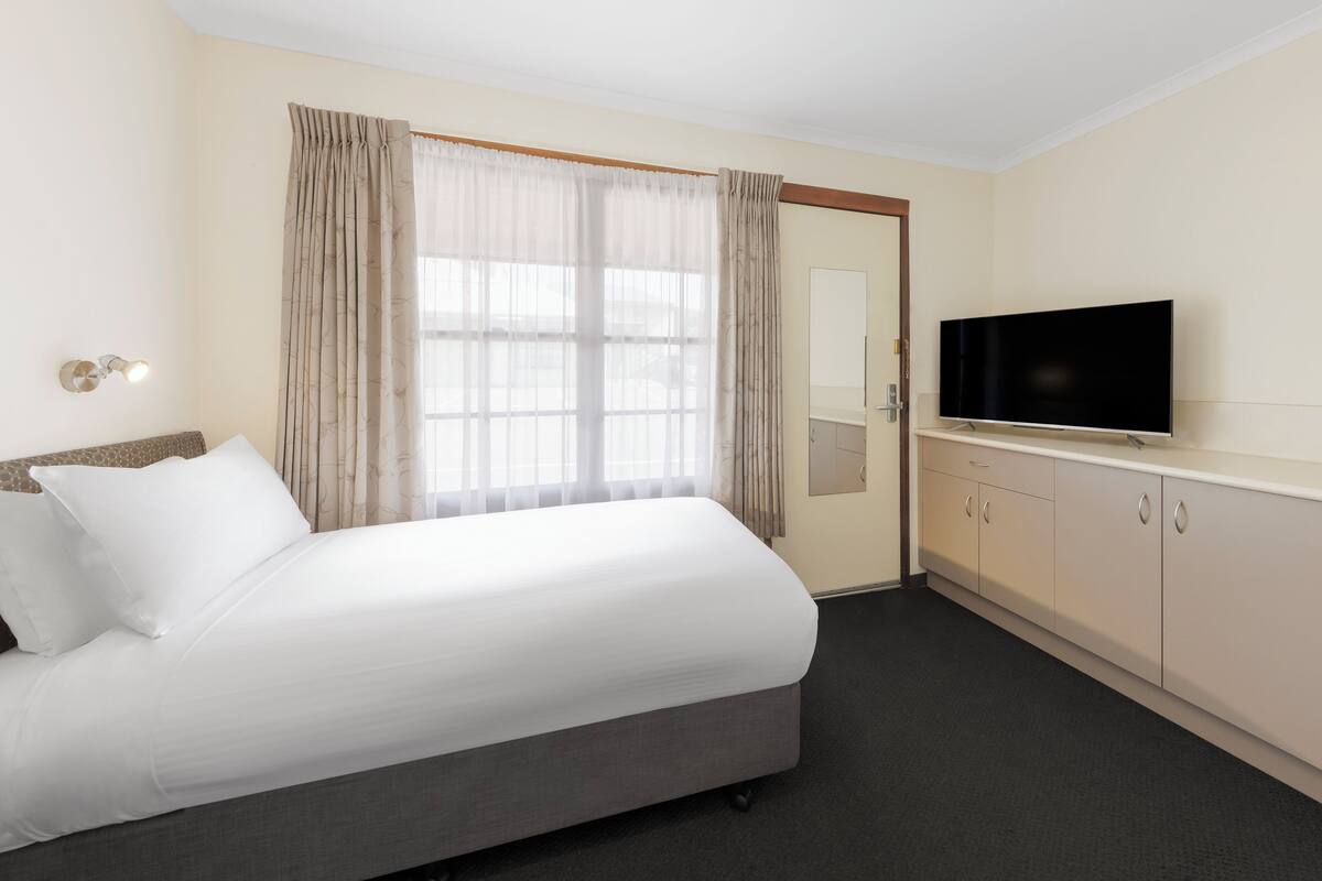 A hotel room with a bed, a television, a wardrobe, and a window with curtains.