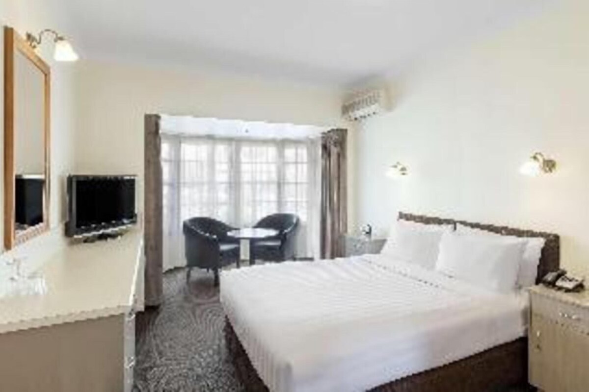 A hotel room with a bed, a TV, a desk, and a chair.