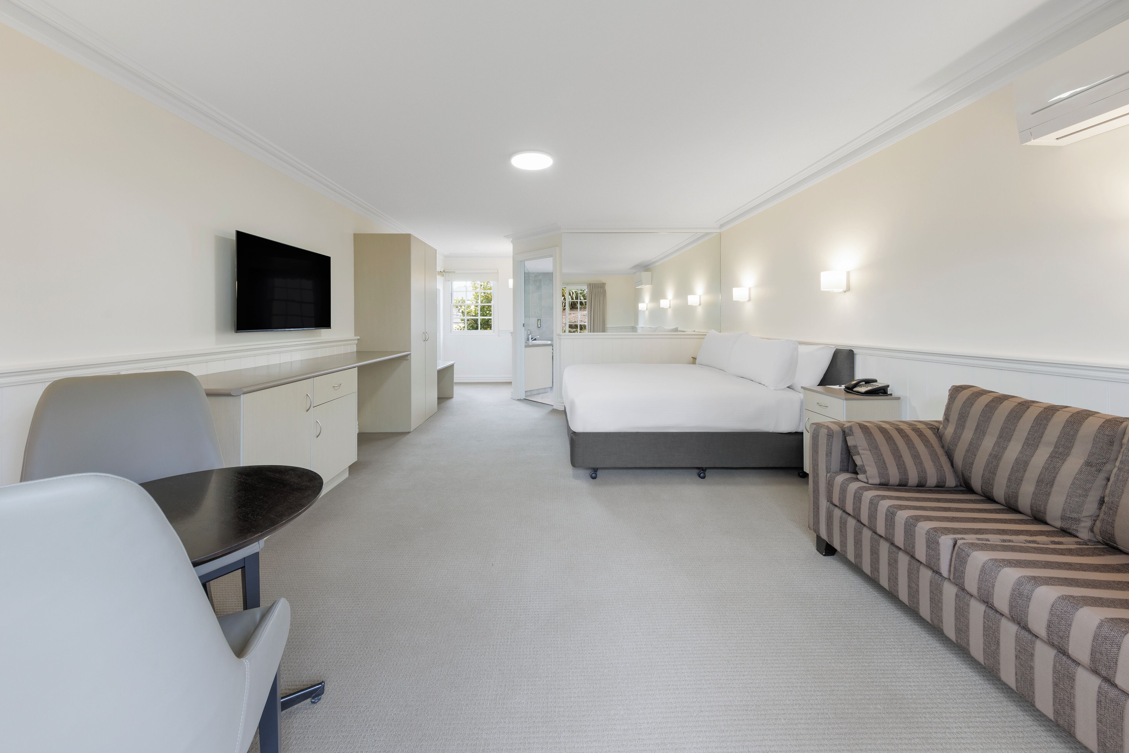 Une chambre d’hôtel comprenant un lit, un canapé, un bureau avec une chaise, une télévision et une salle de bain visible à travers une porte ouverte.