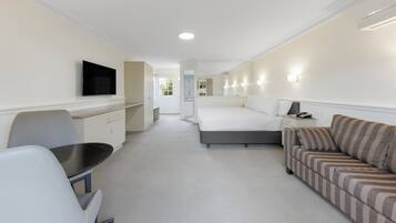 Une chambre d’hôtel comprenant un lit, un canapé, un bureau avec une chaise, une télévision et une salle de bain visible à travers une porte ouverte.