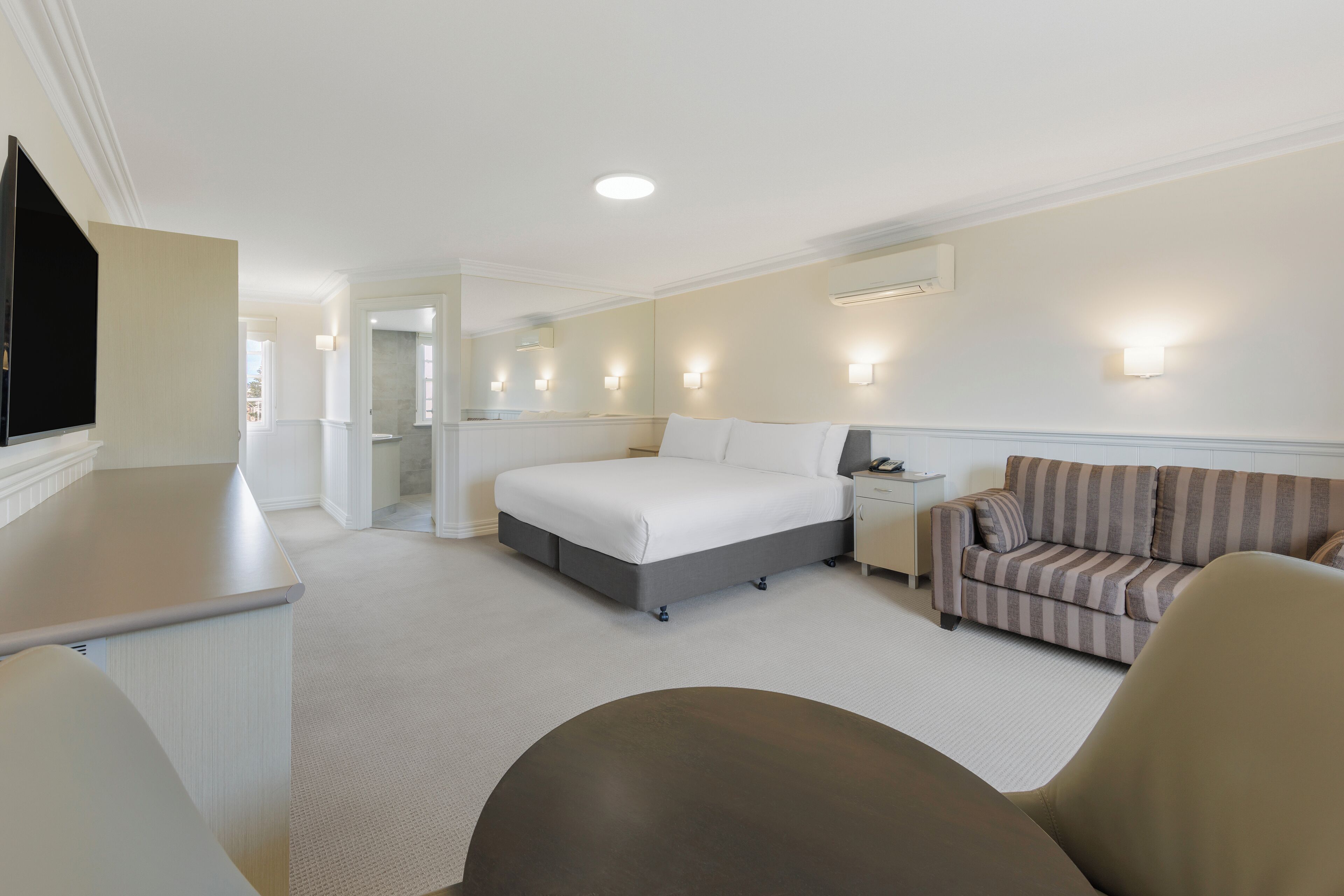 A hotel room with a bed, a sofa, a desk, and a television.