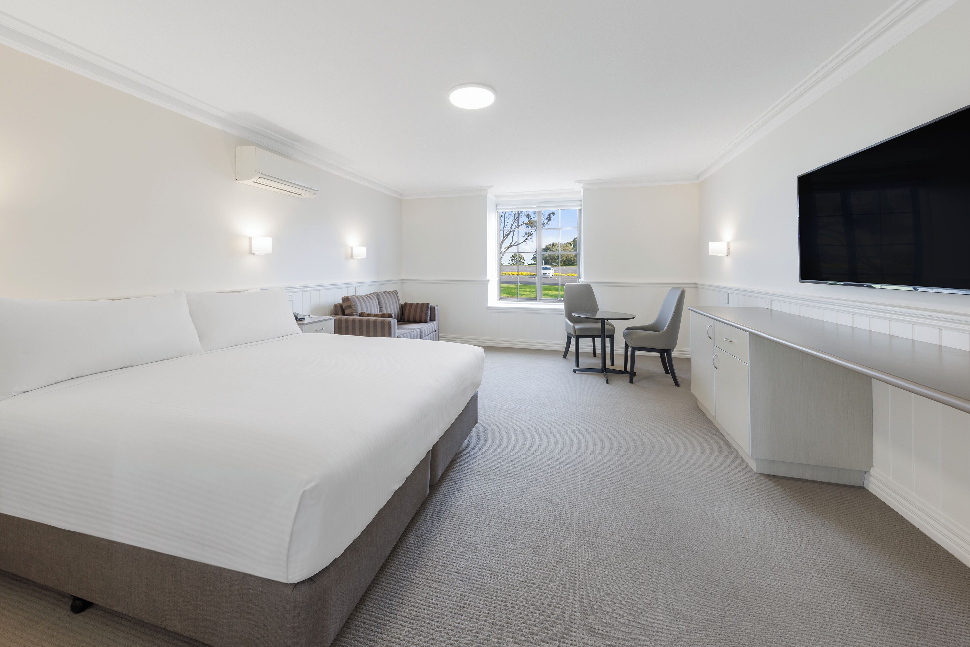 A hotel room with a large bed, a desk, a chair, and a TV.