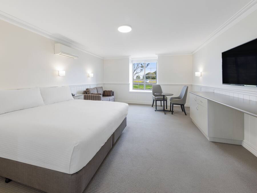 A hotel room with a large bed, a desk, a chair, and a TV.
