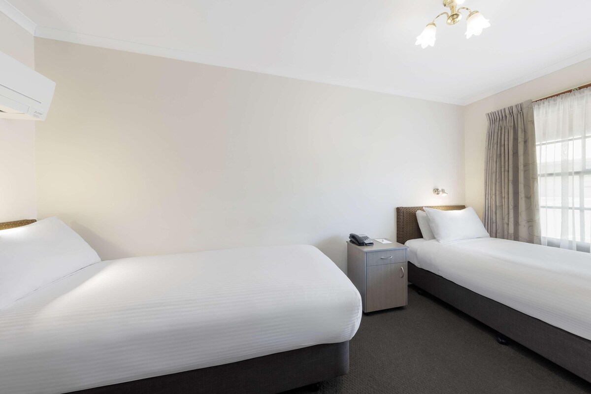 A hotel room with two beds, a bedside table with a phone, a small cabinet, and a ceiling light fixture.