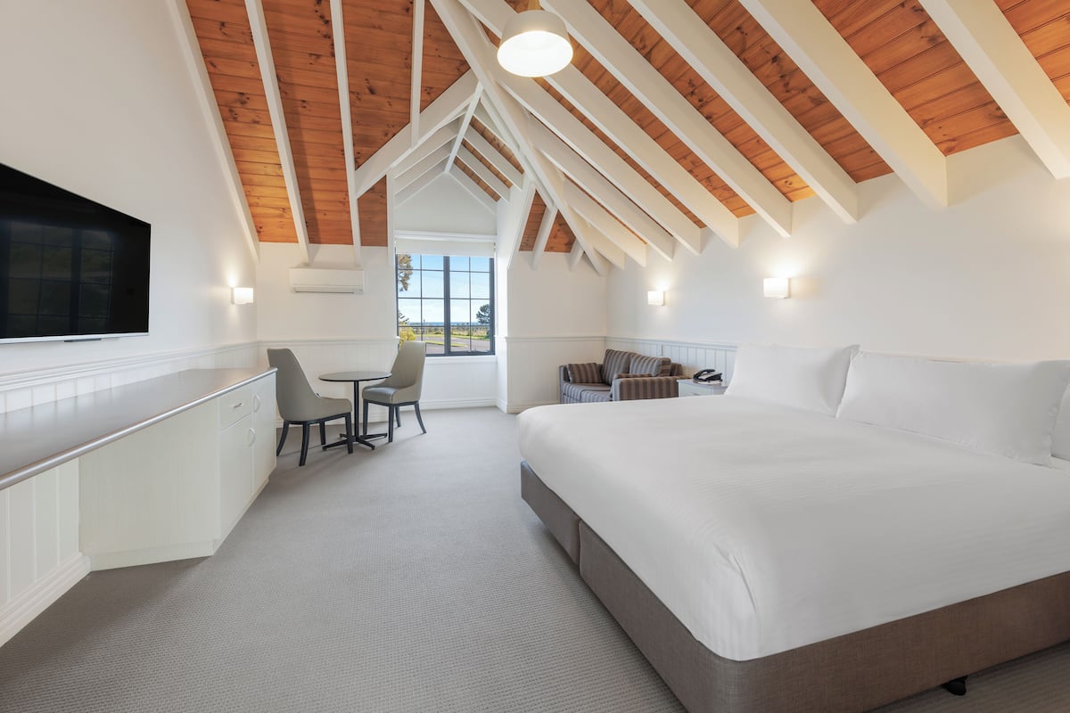 A modern bedroom with a large bed, a desk, and a chair. There is a window with a view of the outdoors.