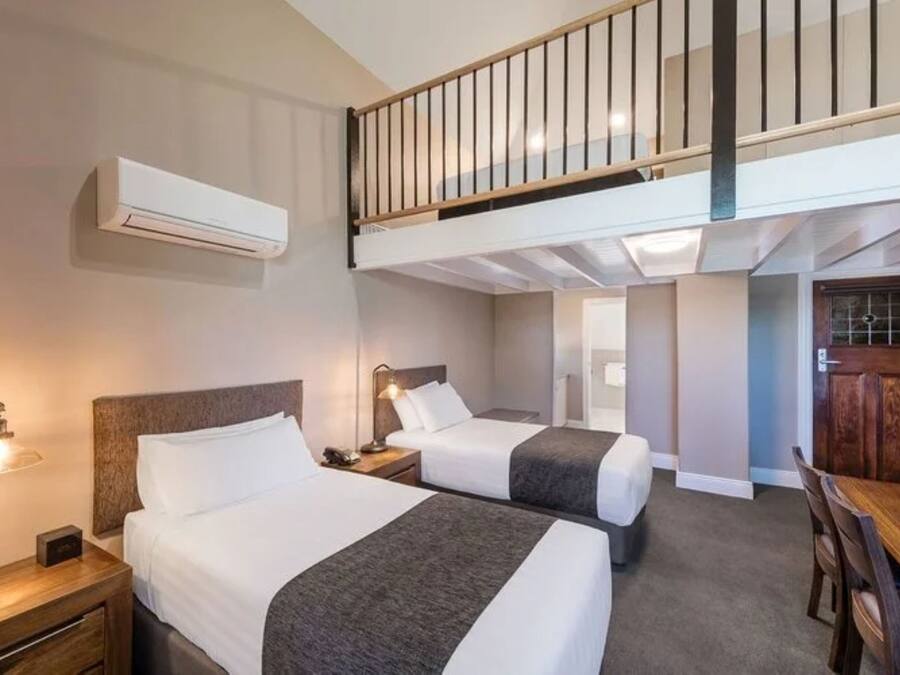 Een hotelkamer met twee bedden, een bureau, een stoel, een trap en een airconditioner.