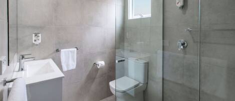 Un baño moderno con cabina de ducha de vidrio, lavamanos blanco y retrete.
