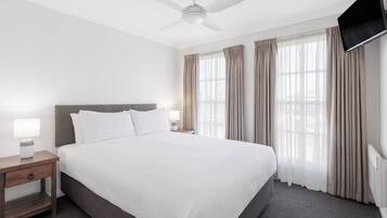 Habitación de hotel con una cama grande, una mesita de noche con lámpara, ventilador de techo y televisor montado en la pared.