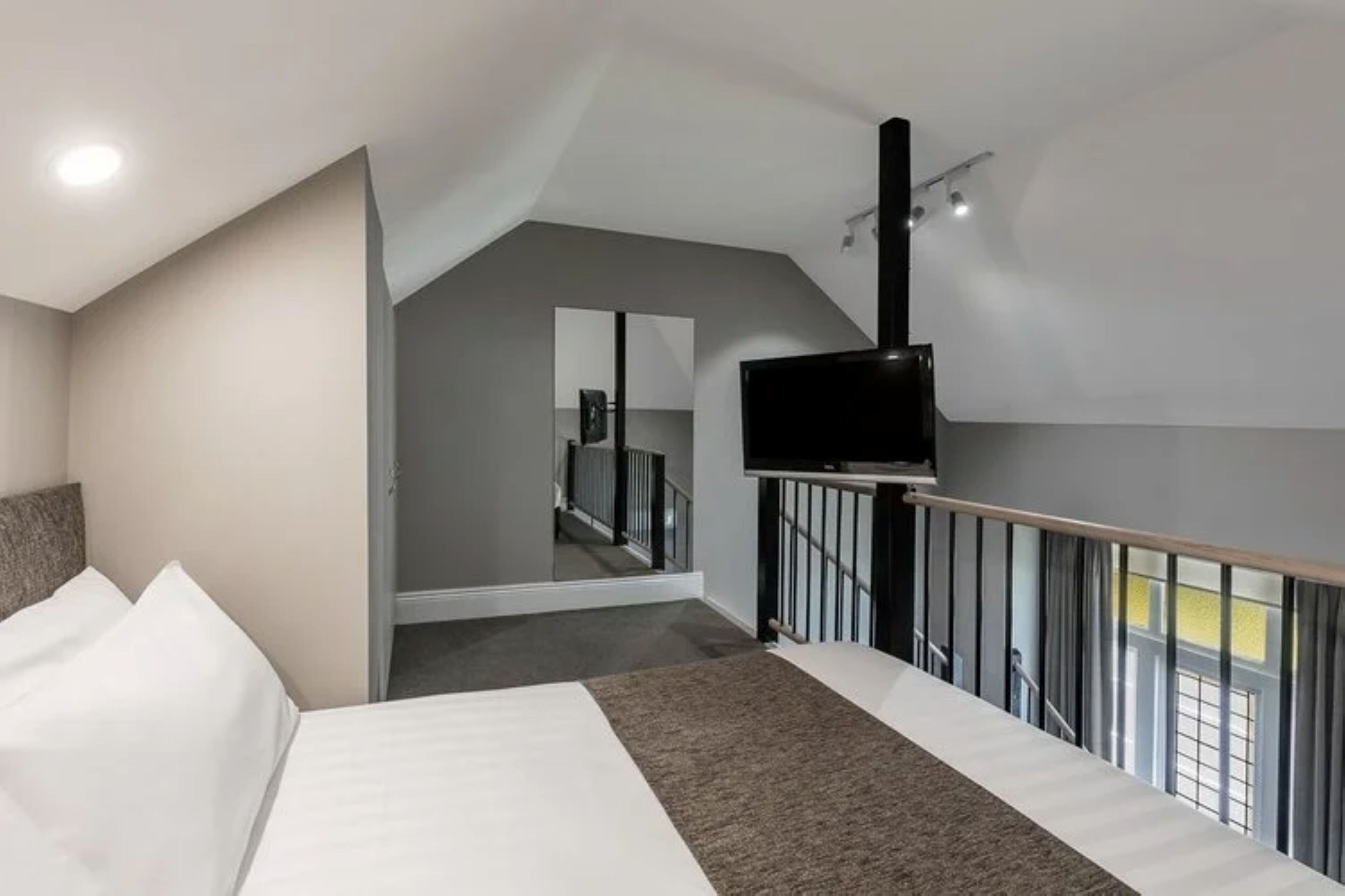 Une chambre d’hôtel moderne dotée d’un grand lit, d’un téléviseur à écran plat fixé au mur et d’un escalier menant à un niveau supérieur.