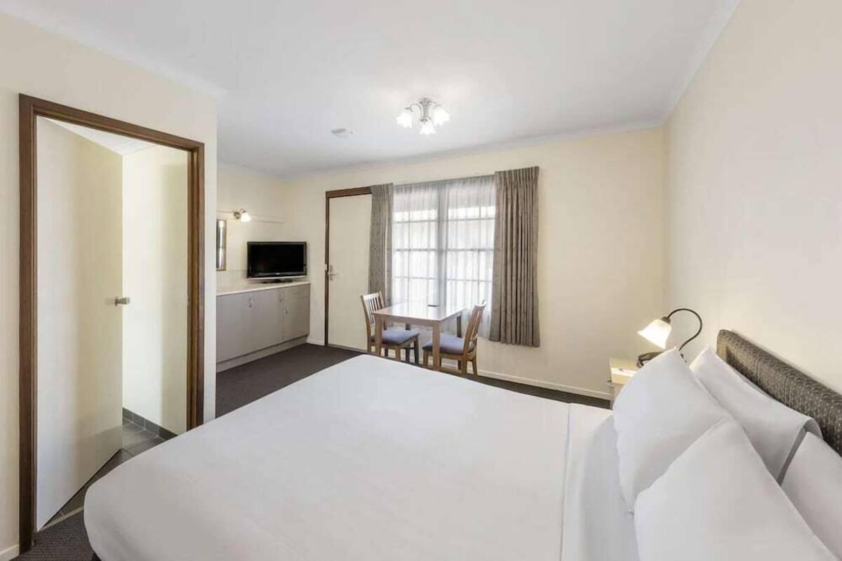 A hotel room with a large bed, a desk with chairs, a television, and a window with curtains.