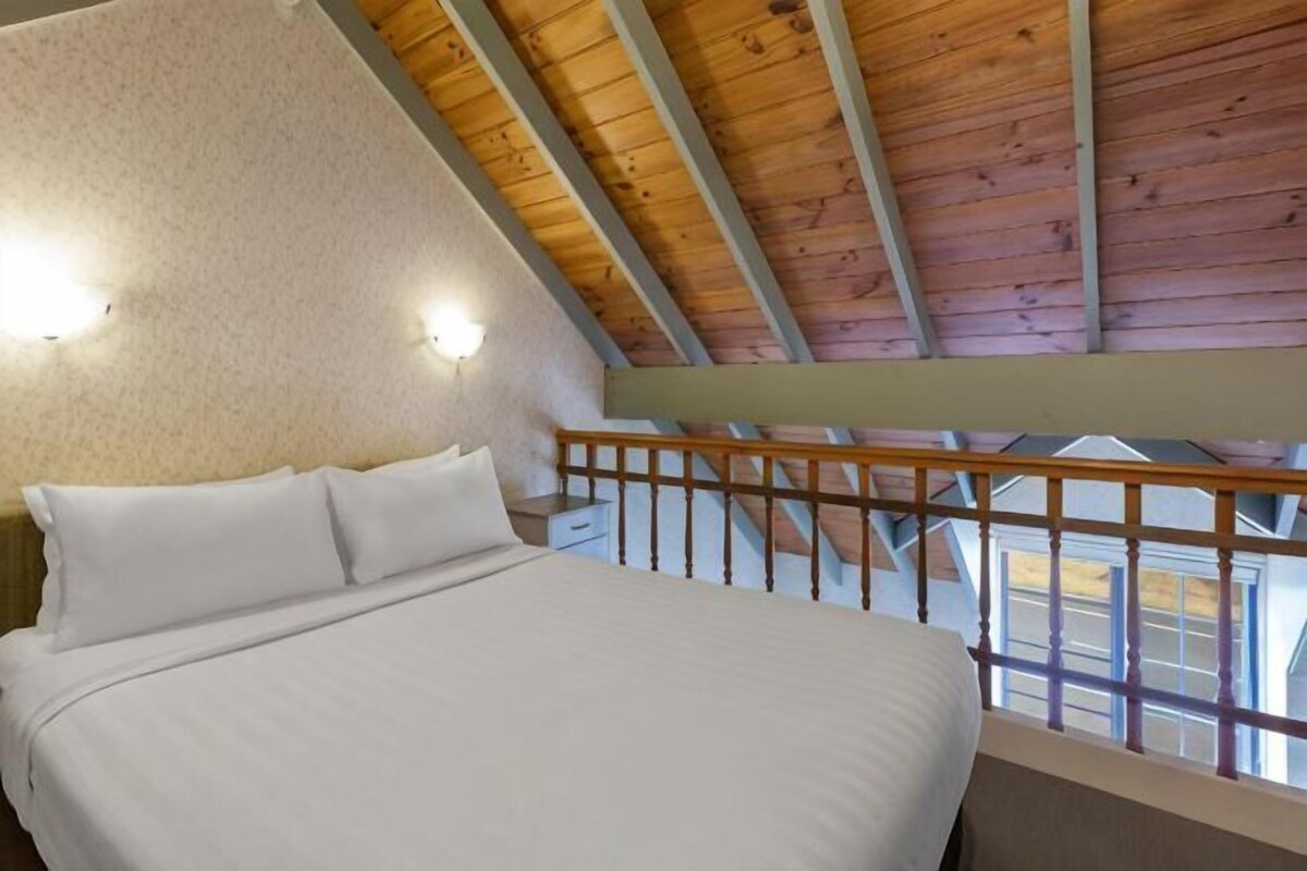 A bedroom with a wooden ceiling, a bed with white linens, and a balcony with a railing.
