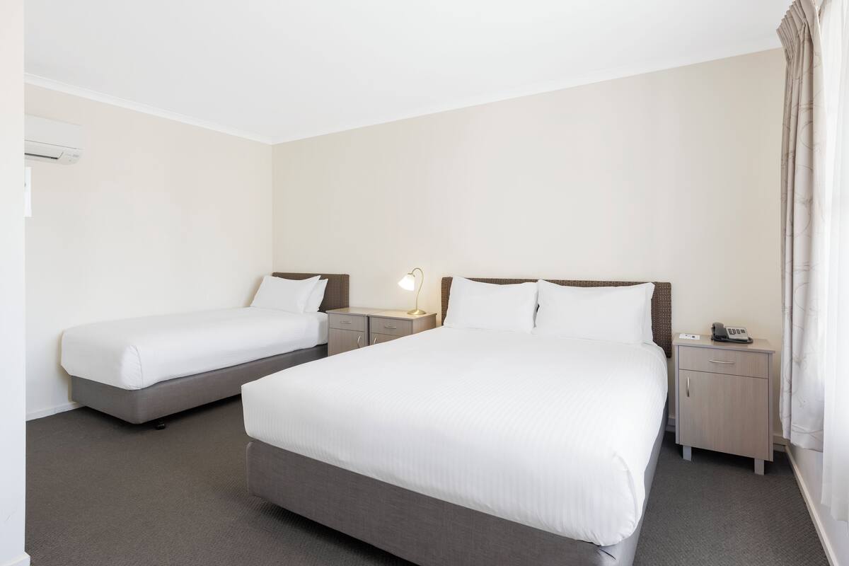 A hotel room with two single beds, a small bedside table with a lamp, a nightstand, and a telephone.