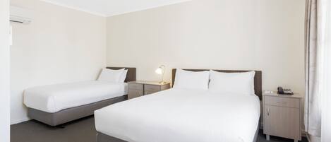 Una habitación de hotel con dos camas individuales, una mesita de noche con lámpara, una mesita auxiliar y un teléfono.
