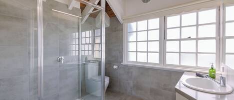 Une salle de bain moderne dotée d’une douche à parois de verre, de toilettes, d’un lavabo avec un miroir et d’une grande fenêtre qui laisse entrer la lumière naturelle.