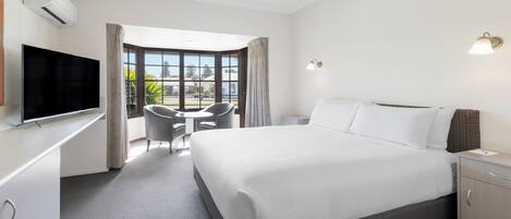 Una habitación de hotel con una cama grande, un escritorio con televisor de pantalla plana, una mesita con dos sillas y una ventana con cortinas.