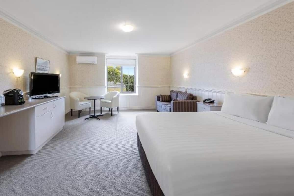 A hotel room with a bed, a desk with a TV, a chair, a small table, and a window.
