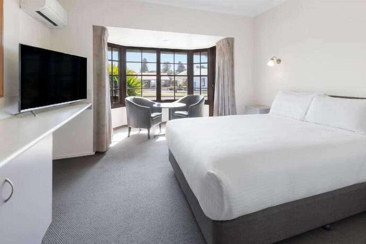 A hotel room with a bed, a TV, a desk, and a chair.