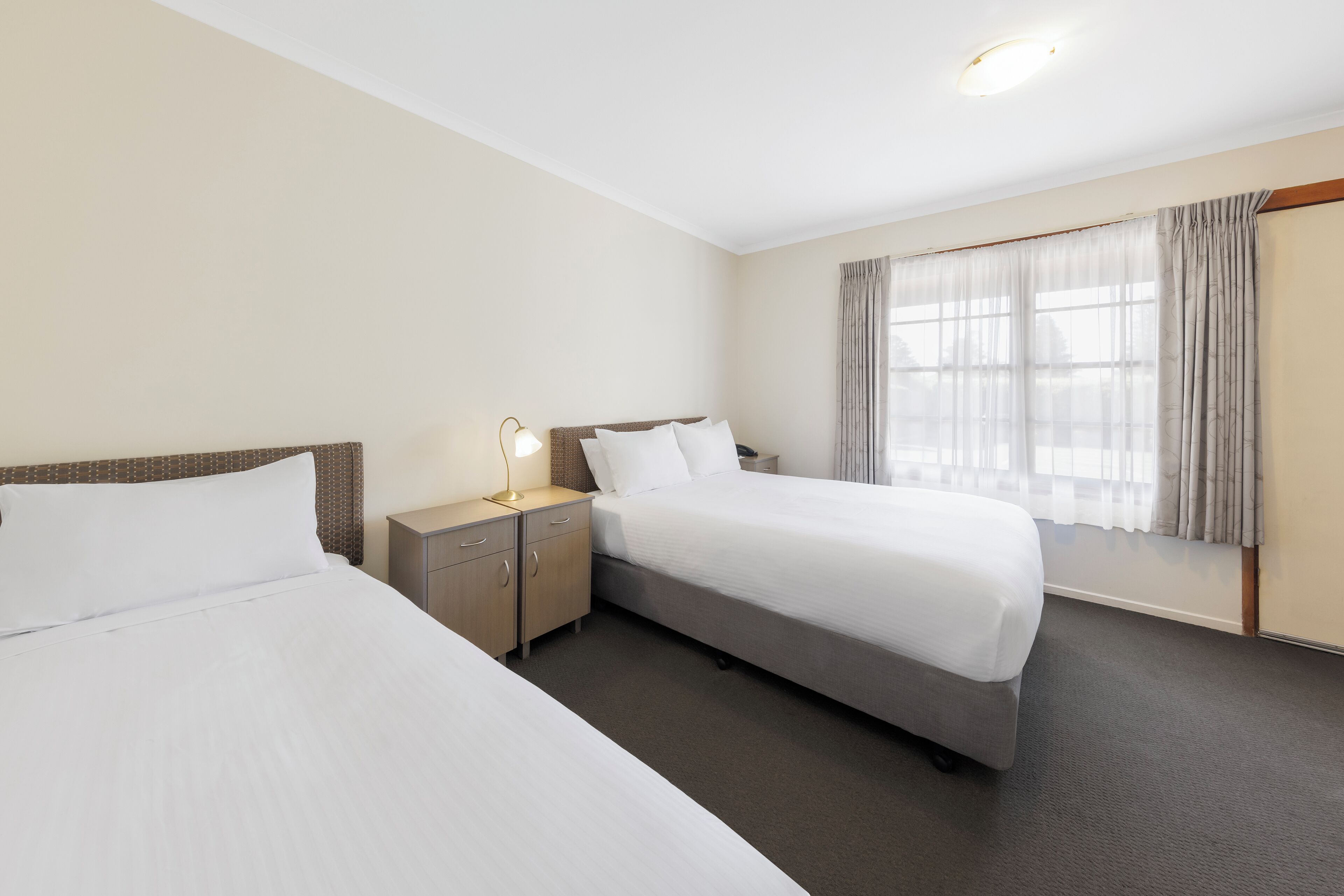 A hotel room with two beds, a nightstand with a lamp, and a window with curtains.
