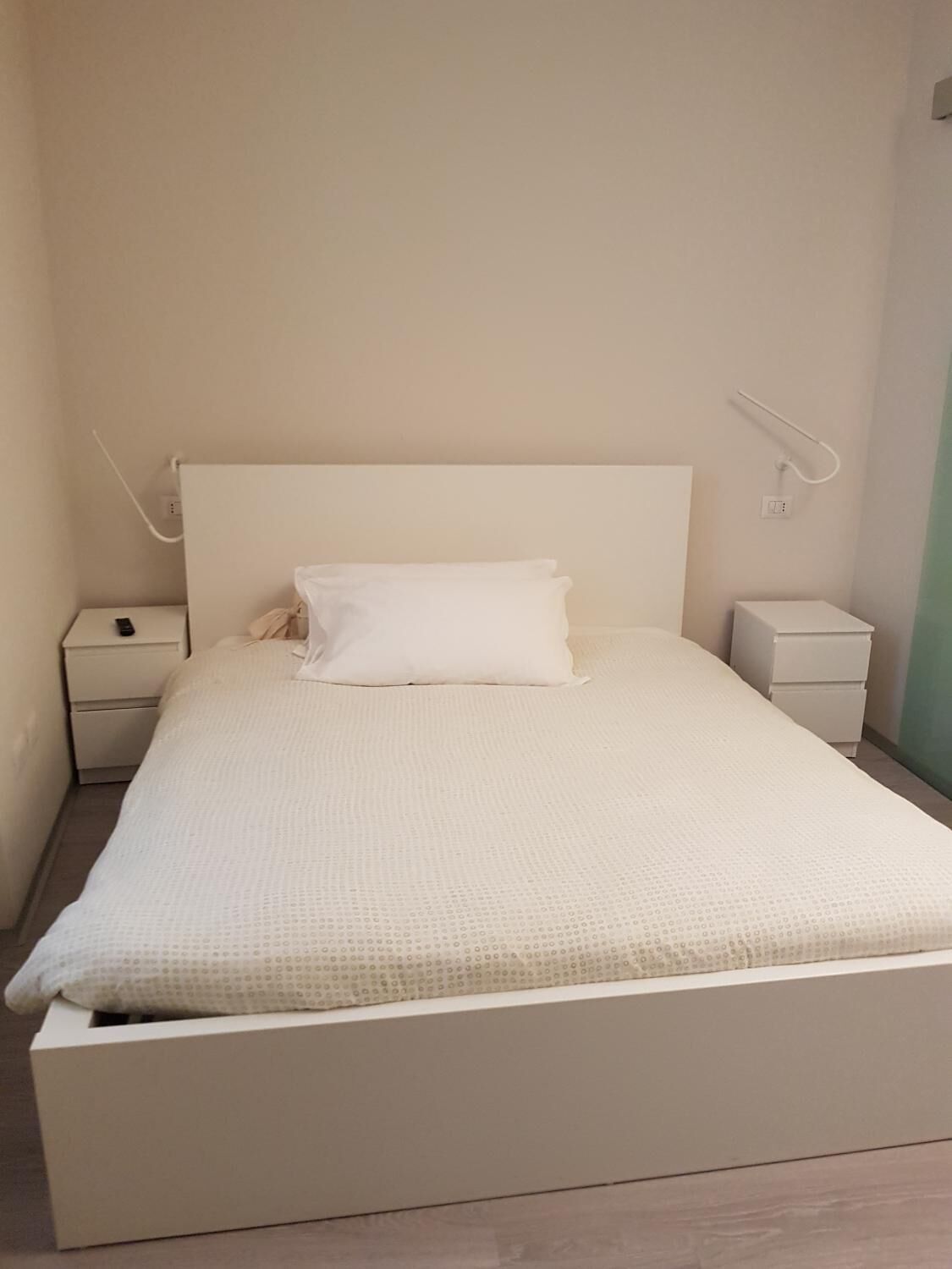 Un dormitorio minimalista con una cama individual, ropa de cama blanca y dos mesitas de noche.