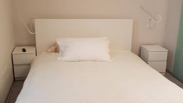 A minimalist bedroom with a single bed, white bedding, and two bedside tables.