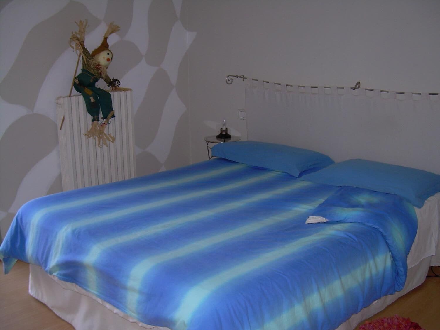 Un dormitorio con una cama cubierta con ropa de cama azul a rayas, un radiador blanco y un objeto decorativo sobre este.