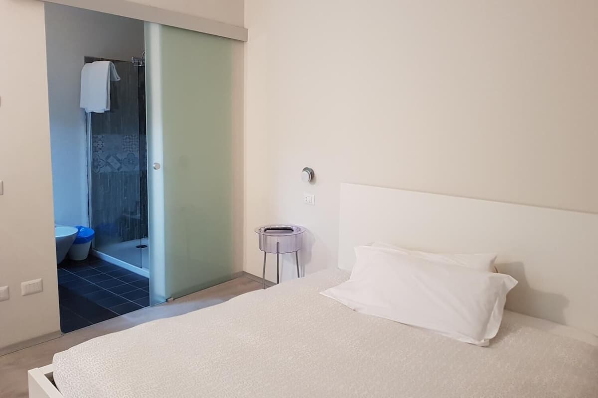 A bedroom with a bed, a bedside table, and a bathroom visible through an open door.