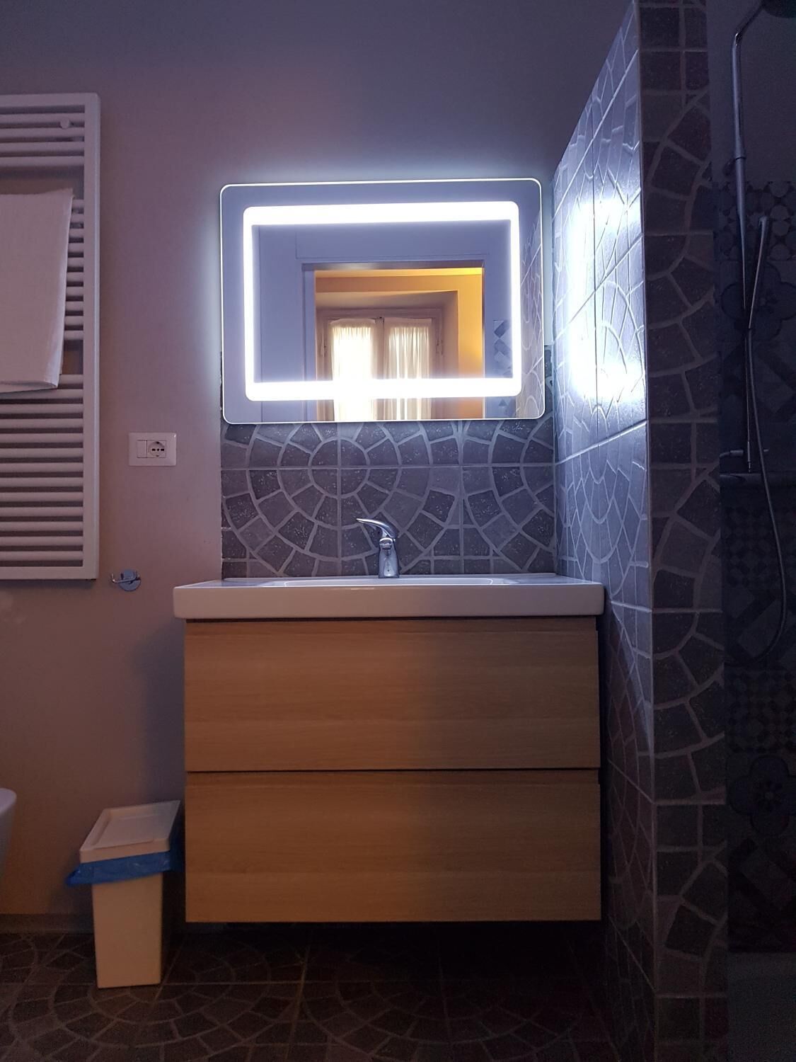 Ein Badezimmer mit einem modernen Waschtisch, einem Spiegel mit integrierter Beleuchtung und Wandfliesen mit Muster.