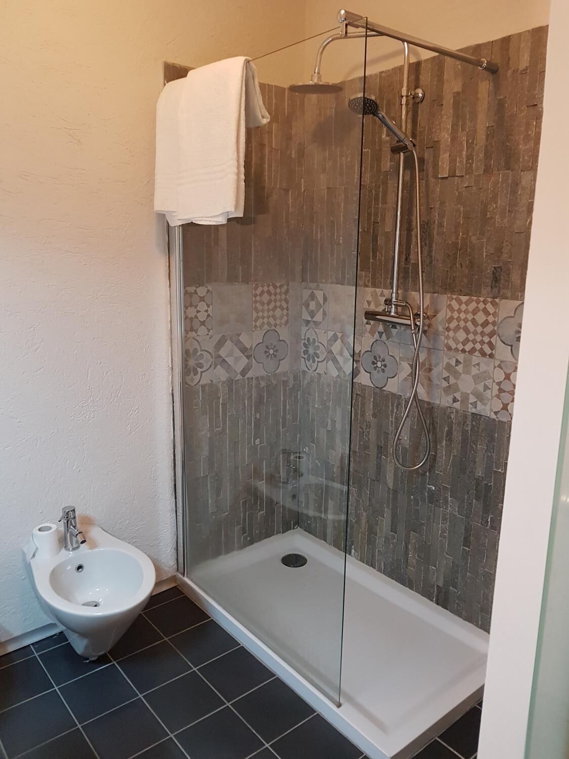 Zona de ducha con mampara de vidrio, una toalla blanca colgada en la puerta y un cabezal de ducha.