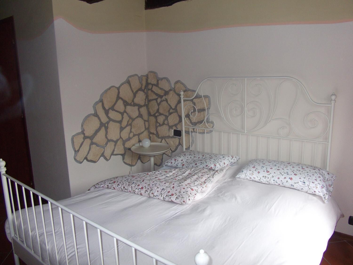 A bed with a white metal frame, two pillows with a floral pattern, and a small bedside table with a white lamp.