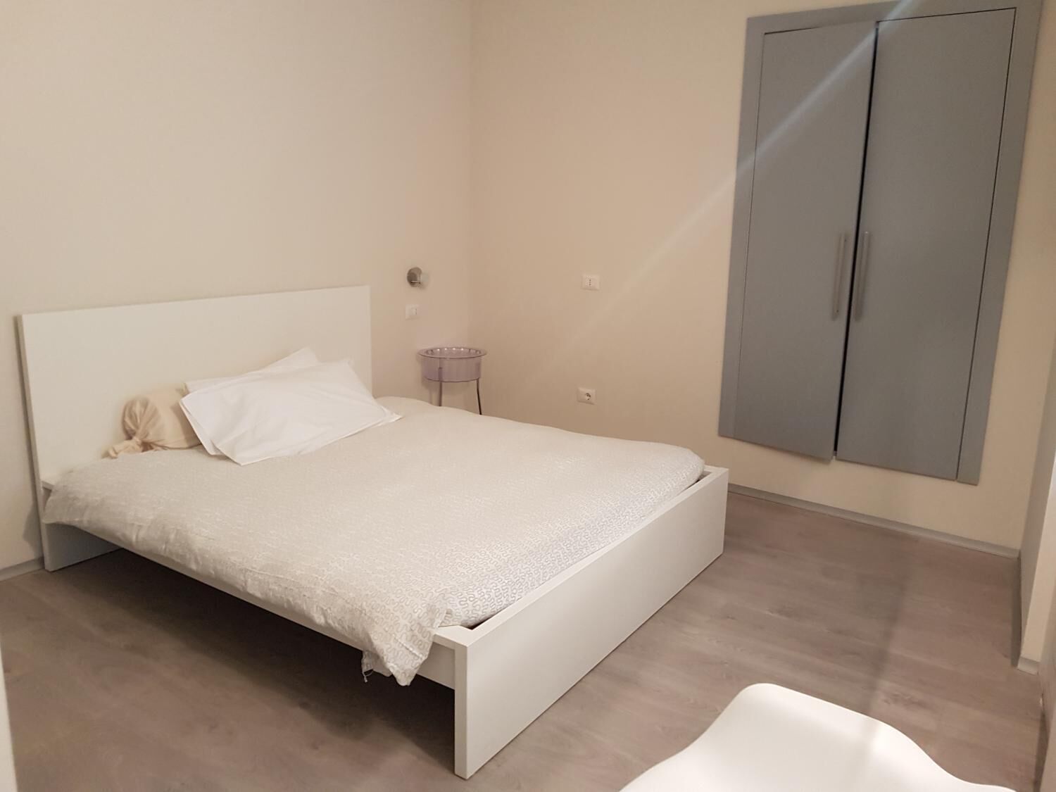 A minimalist bedroom with a bed, a small bedside table, and a wardrobe.