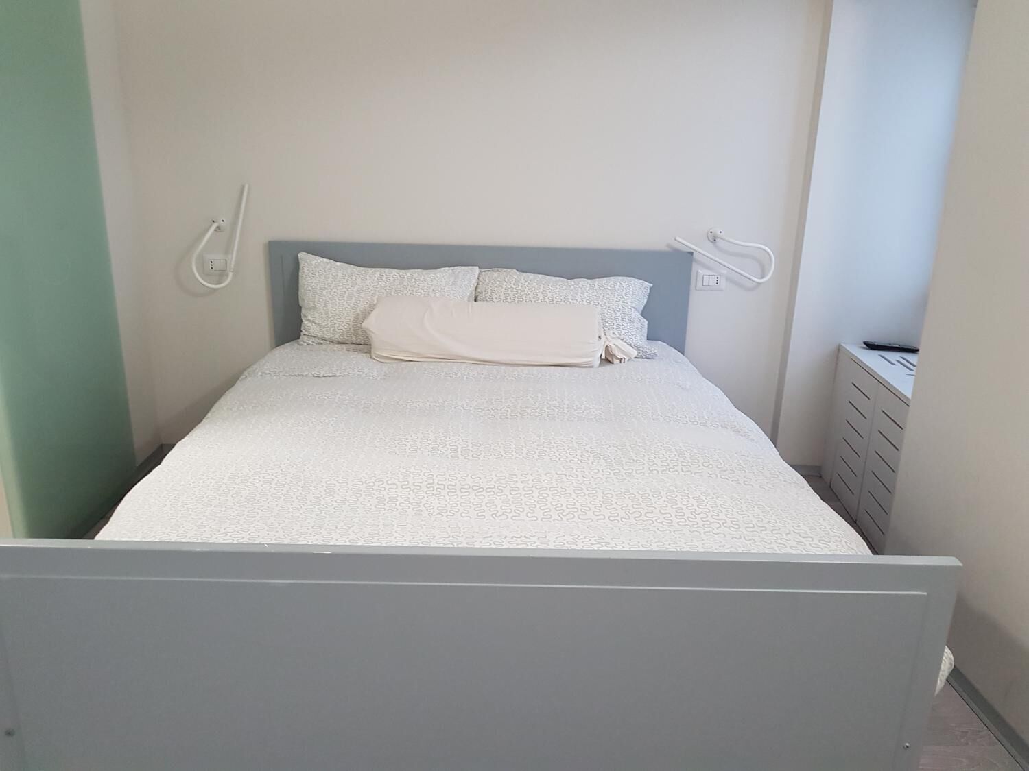 A neatly made bed with a grey headboard, white bedding, and a folded white towel.