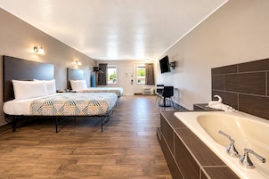 A hotel room with a large bed, a separate bathroom with a bathtub, a desk, and a TV mounted on the wall.