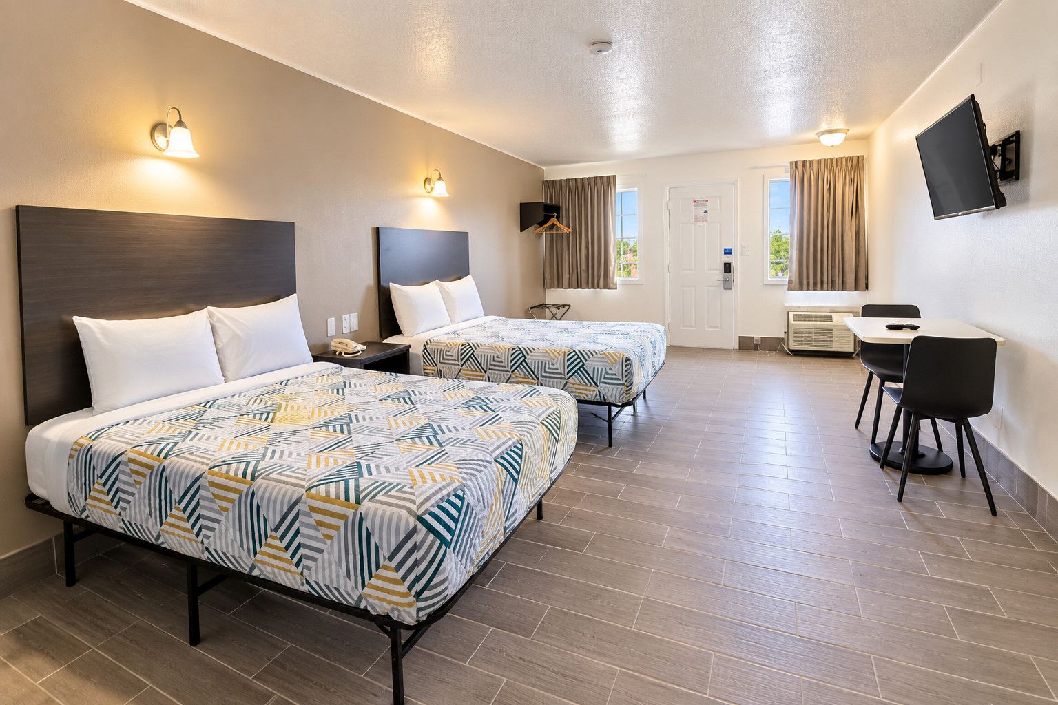 Een hotelkamer met twee bedden, een bureau, stoelen, een televisie en een raam met gordijnen.
