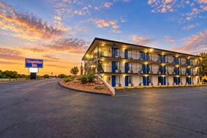 Un motel à plusieurs étages, doté d’un panneau indicateur, d’un parking et d’un espace paysager agrémenté d’arbustes.