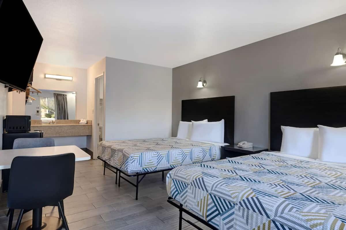 A hotel room with two beds, a desk, a chair, a TV, and a bathroom visible through an open door.